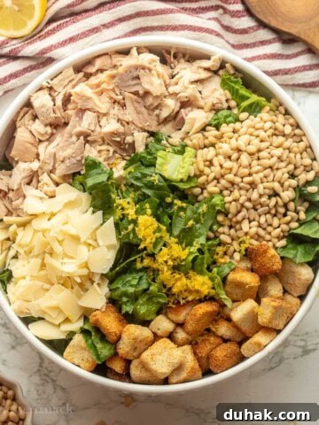 Lemon zest on chicken caesar salad in bowl with wooden spoons.