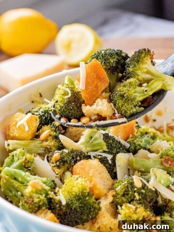 Spoonful of cooked roasted broccoli salad above blue bowl.