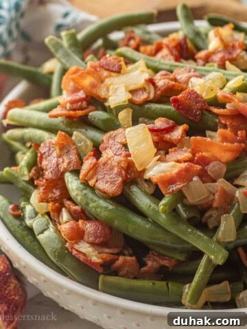 Bowl of cooked green beans with crispy bacon and cooked onions.