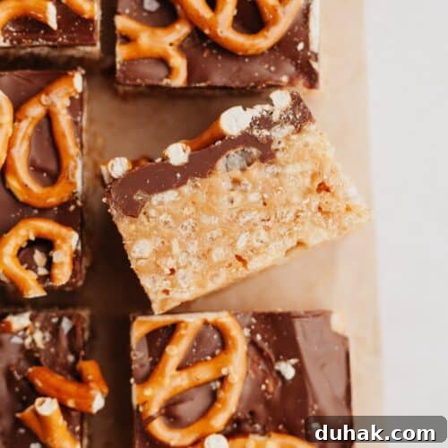 Pretzel topped chocolate peanut butter rice krispie treats on parchment paper, one is on it's side.