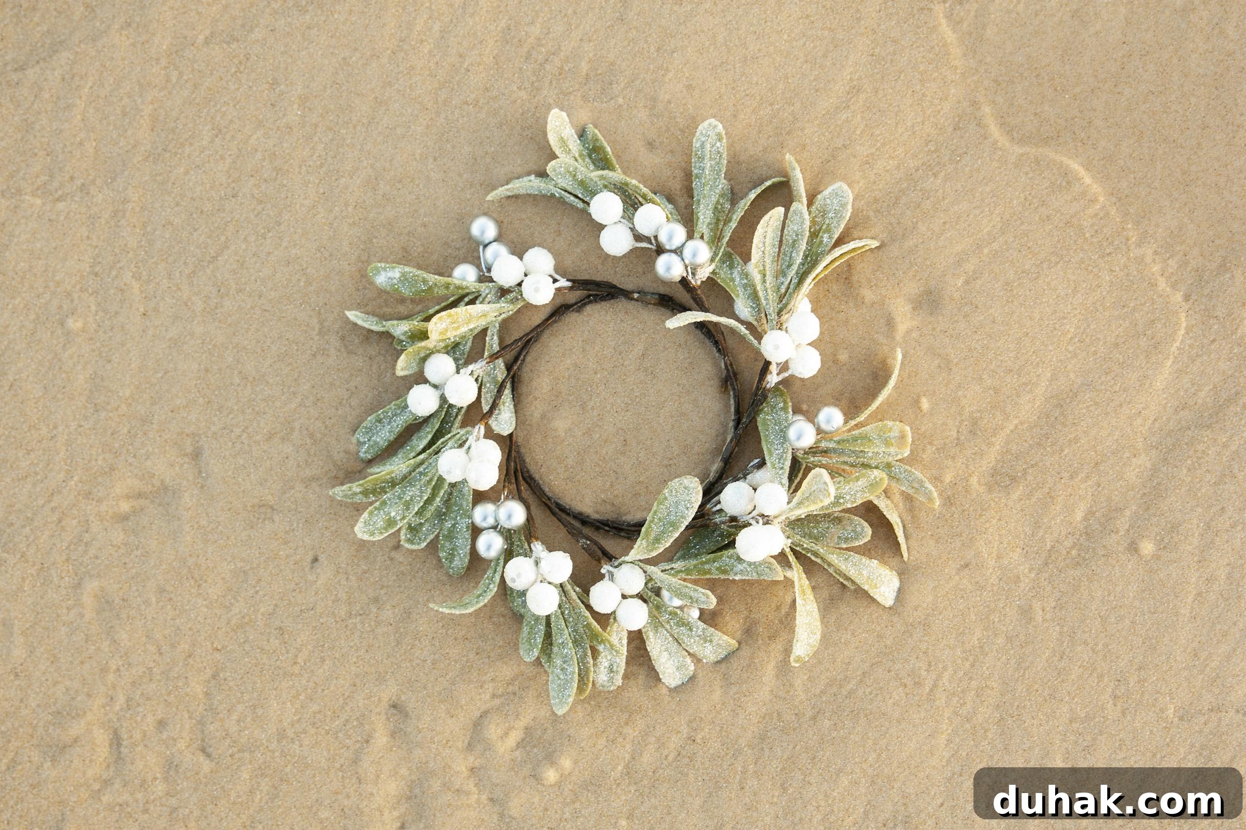Festive Christmas wreath with white berries on a sandy beach. Perfect for seasonal and holiday themes