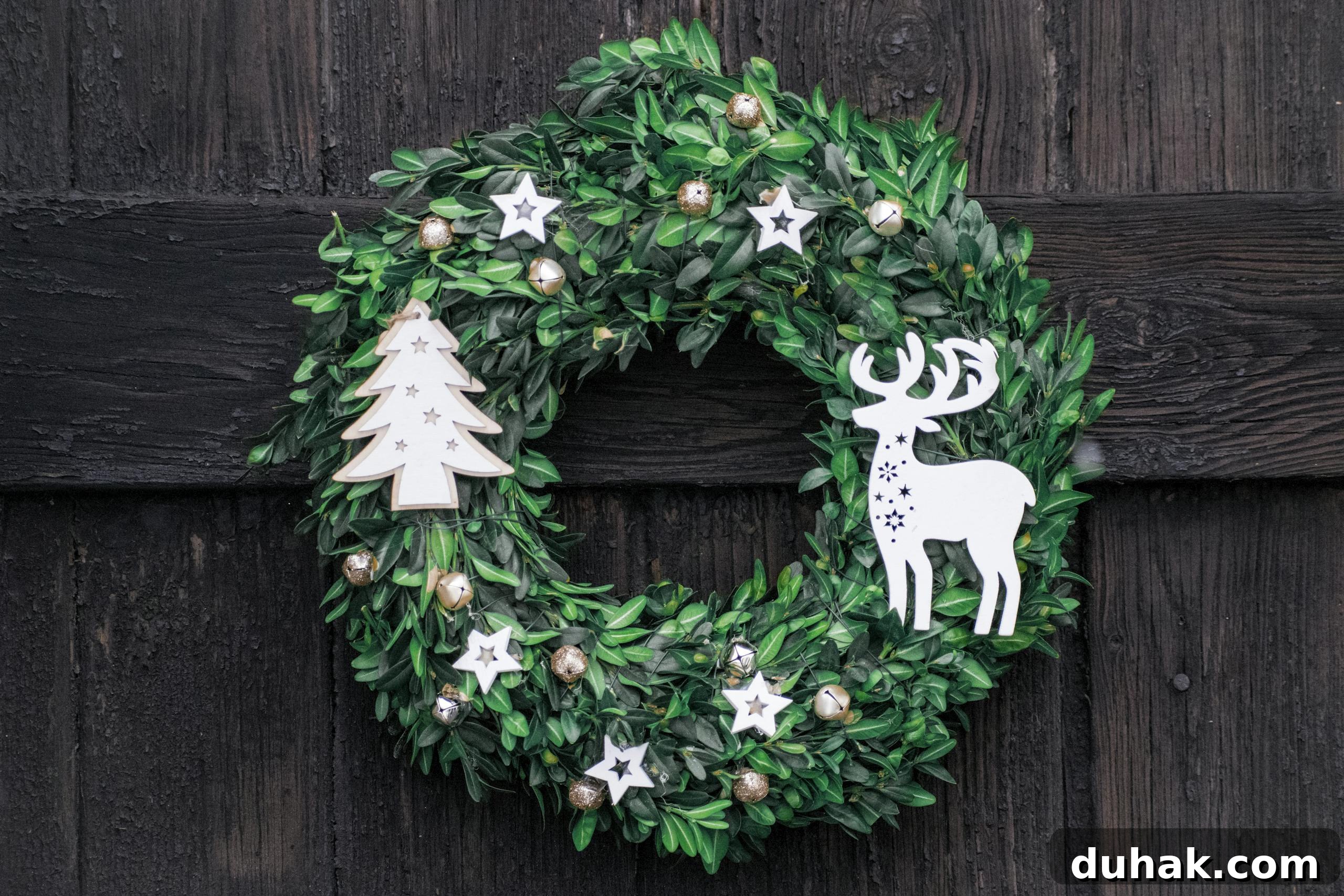 Beautiful green Christmas wreath with deer and tree decoration on a rustic wooden door.