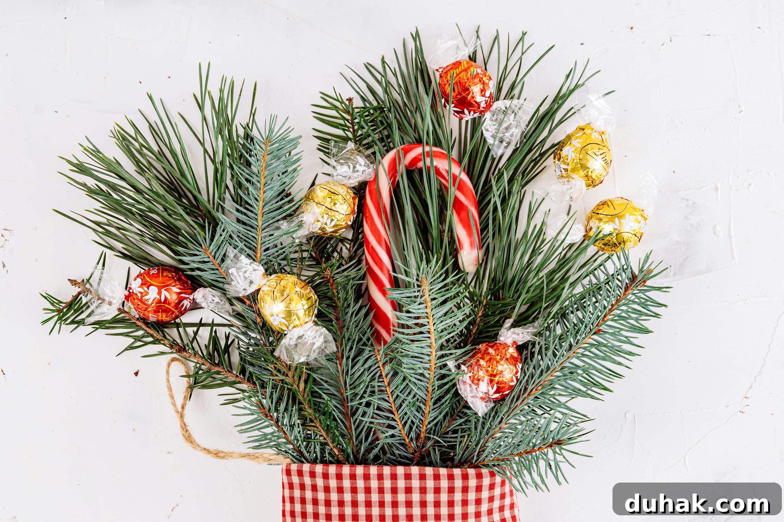 A festive arrangement of pine boughs with candy canes and wrapped chocolates on a white background.