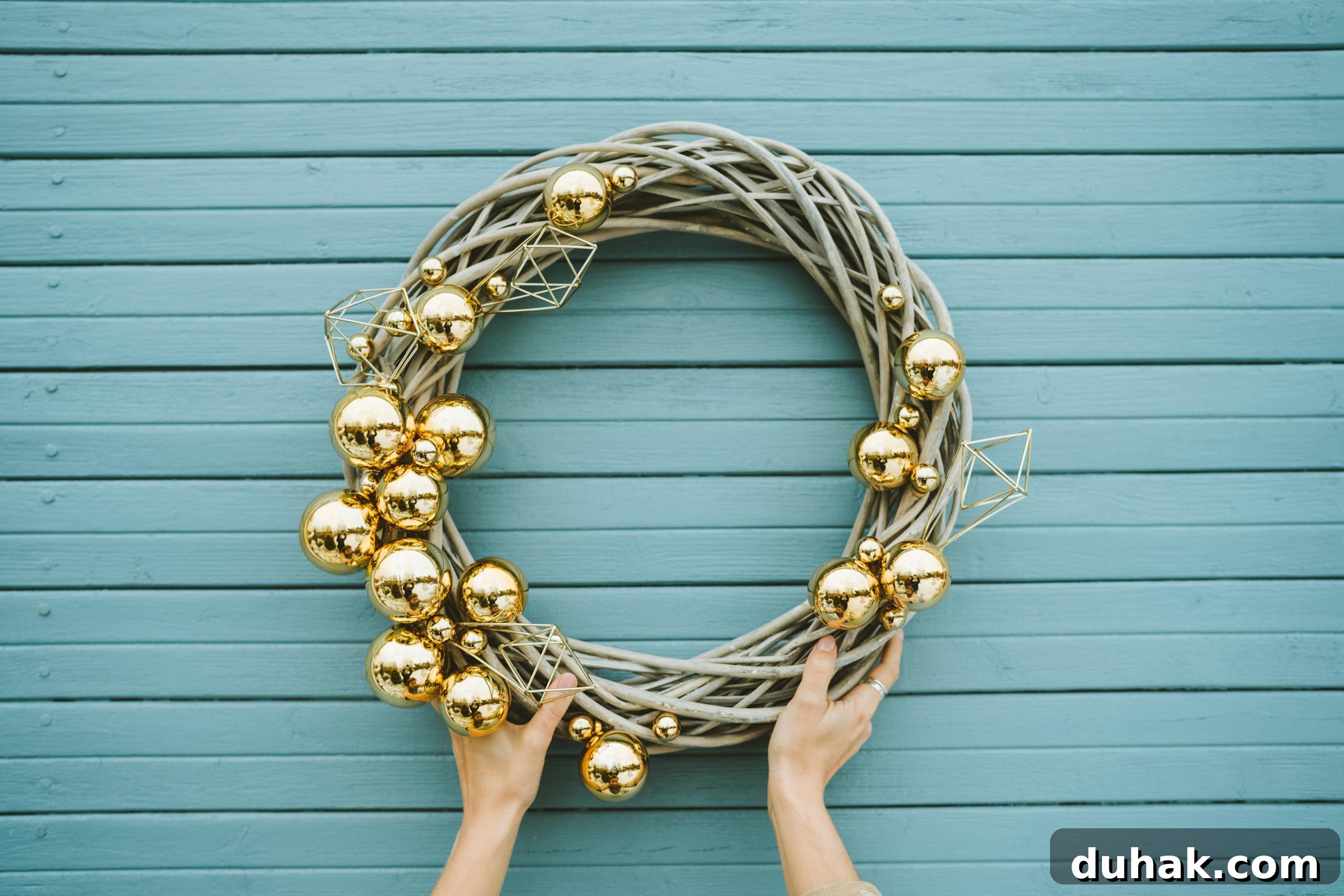Hand holding an elegant Christmas wreath decorated with golden ornaments against a blue wooden background.