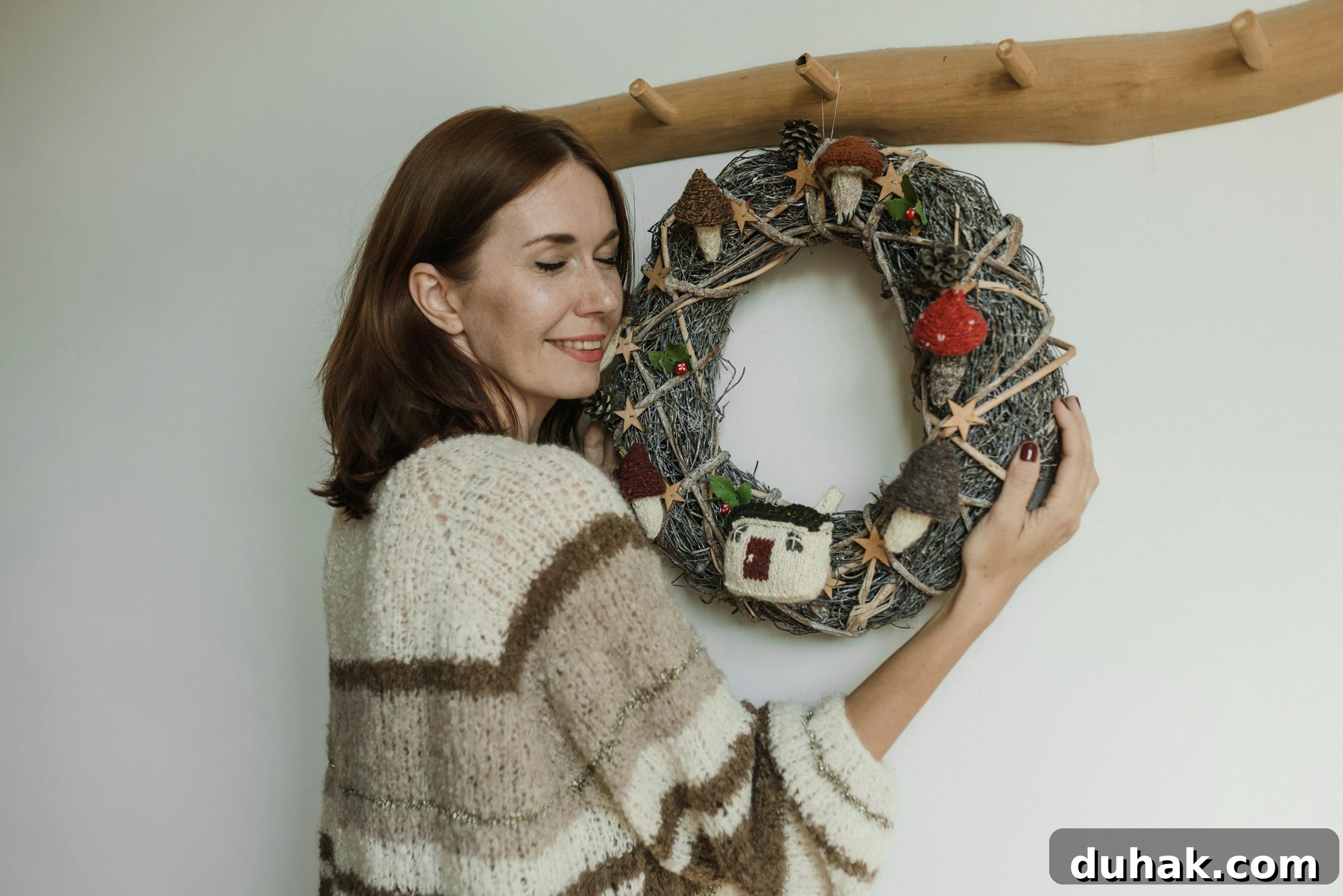 A woman joyfully embraces a rustic handmade wreath decorated with knitted elements and natural textures.