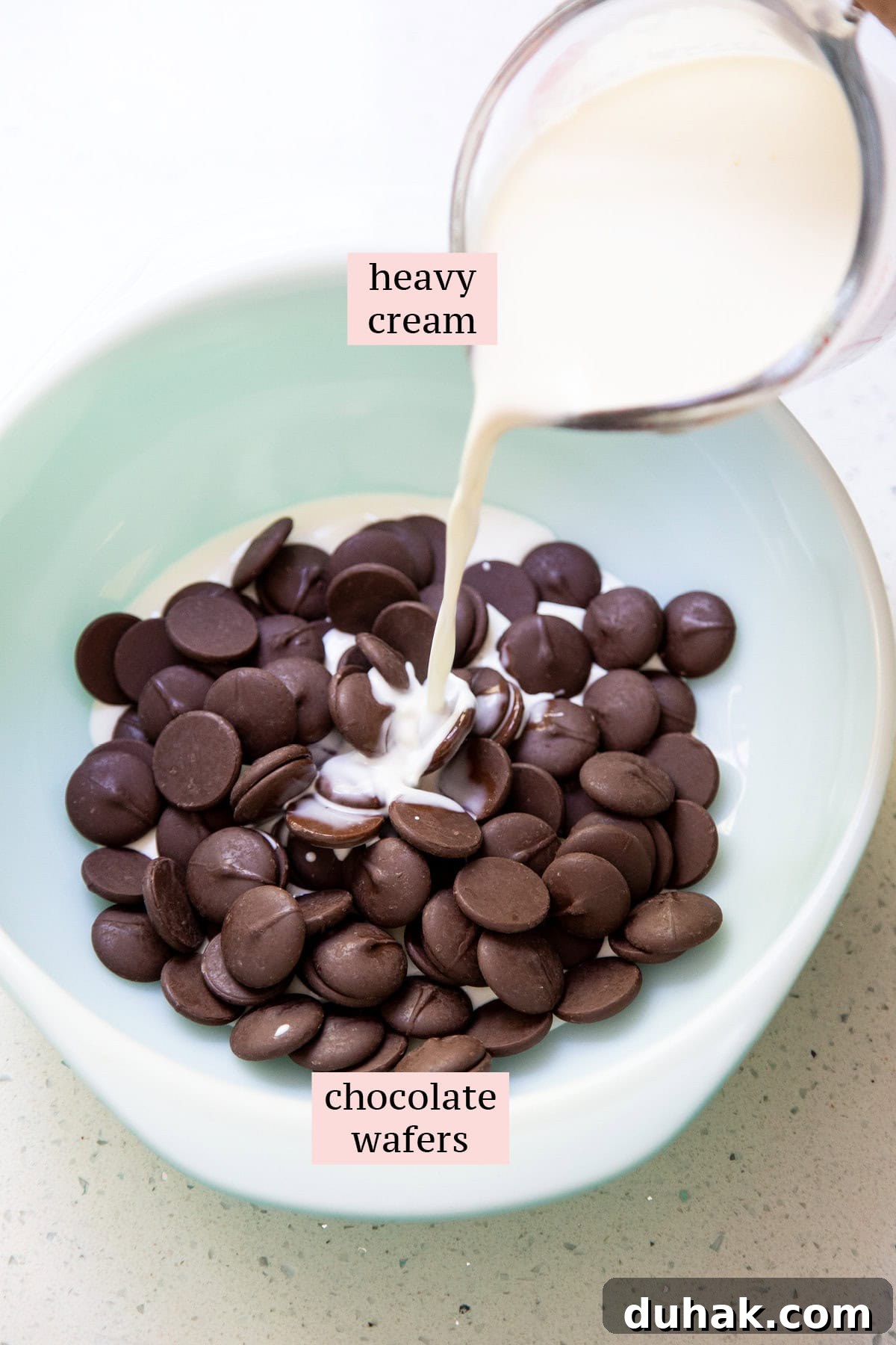 Heavy cream in a measuring cup is pouring into a bowl of chocolate.