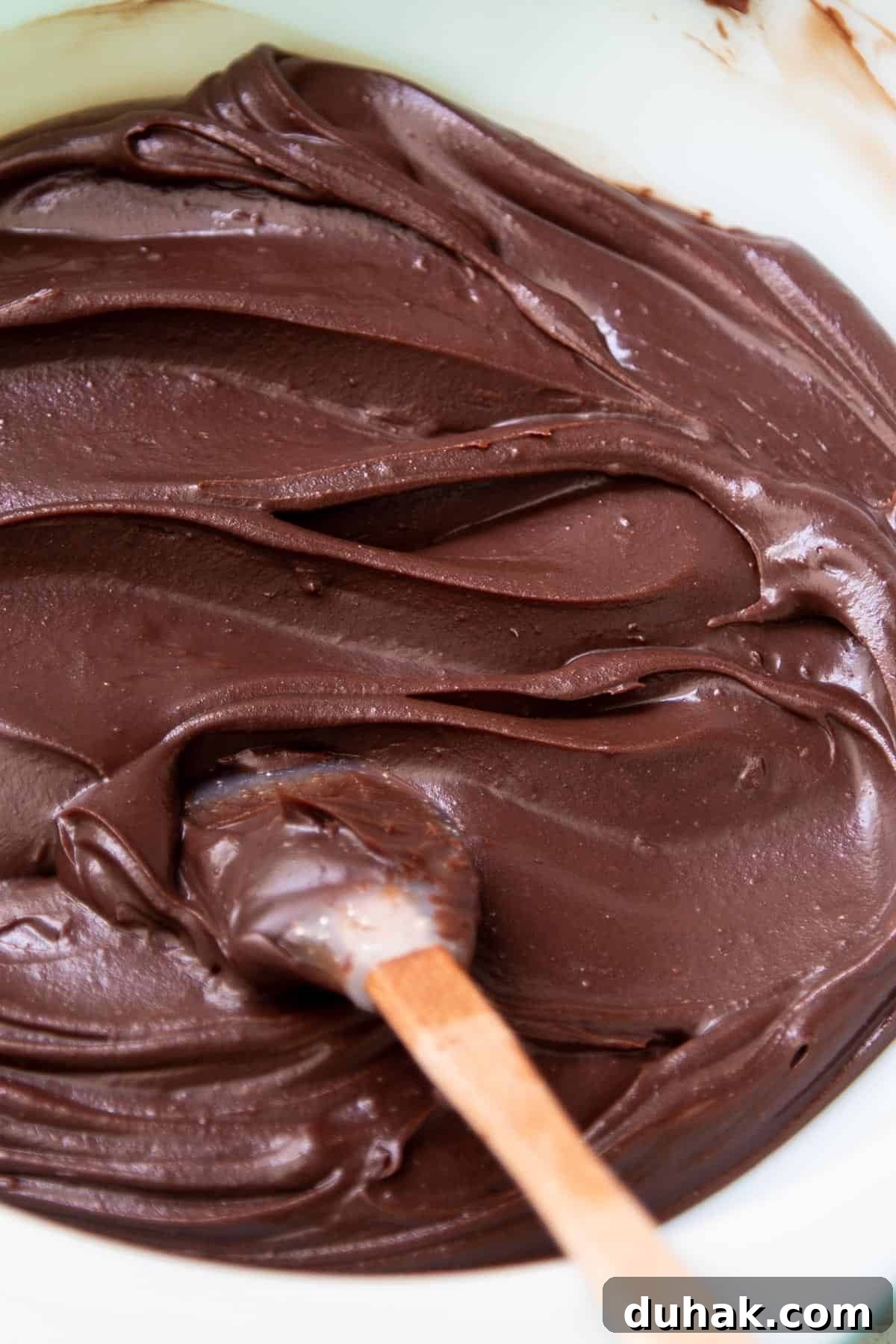 Chocolate ganache frosting in a mixing bowl with a small spatula in it.