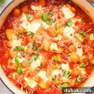 Sorrento-Style Gnocchi with Tomato, Basil & Mozzarella 13 A pot of gnocchi alla sorrentina, smothered in tomato sauce, topped with melted cheese and fresh basil. A wooden spoon, grated cheese bowl, and olive oil stand ready nearby.