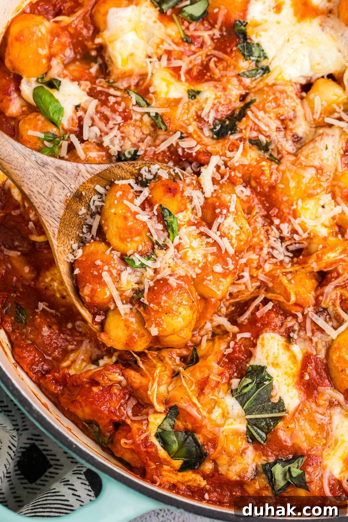 Sorrento-Style Gnocchi with Tomato, Basil & Mozzarella 4 A close-up of a wooden spoon dipping into a pan of gnocchi sorrentina, featuring cheesy baked gnocchi topped with tomato sauce, shredded cheese, and fresh basil.