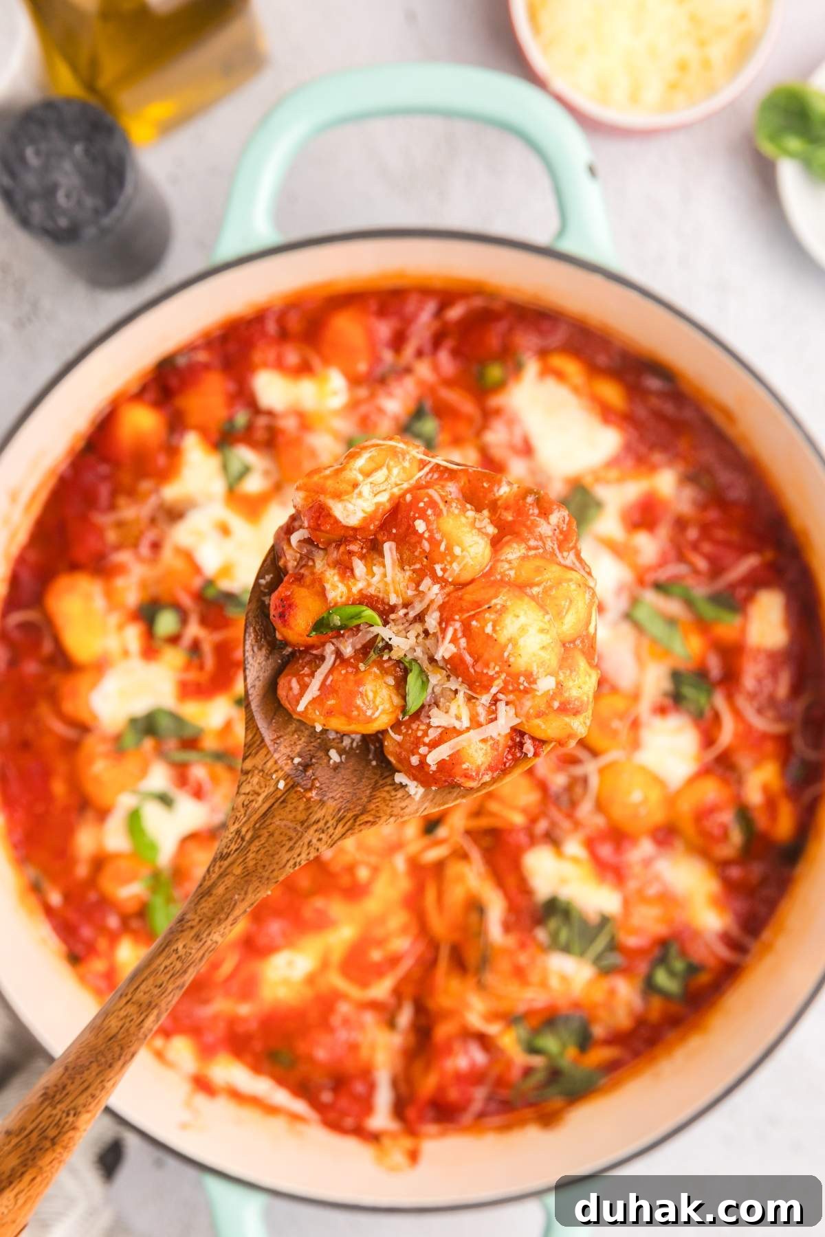 Sorrento-Style Gnocchi with Tomato, Basil & Mozzarella 7 A wooden spoon holding Sorrento style gnocchi with San Marzano tomato sauce, cheese, and basil hovers over a pot of the same delicious dish.