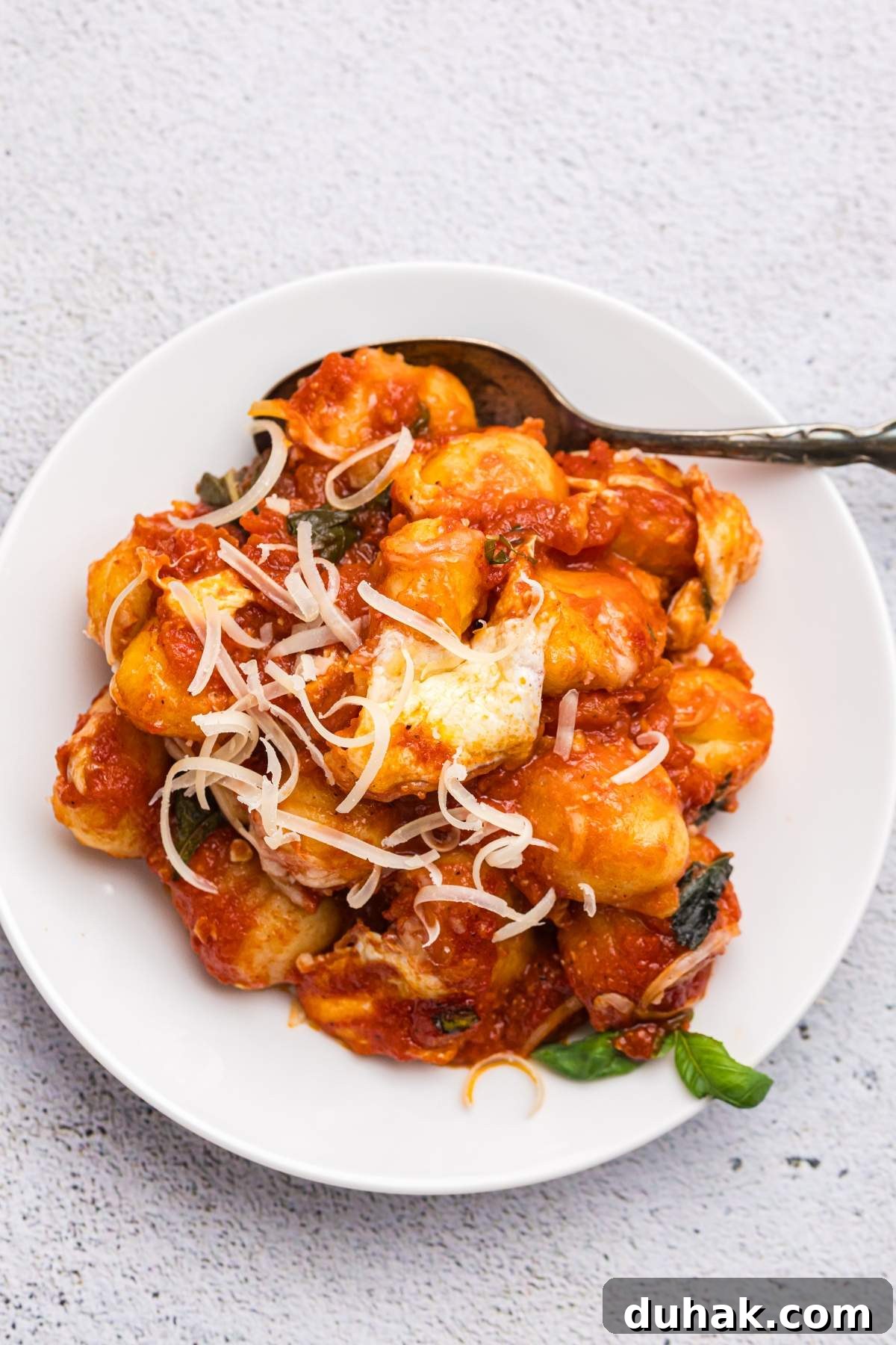 Sorrento-Style Gnocchi with Tomato, Basil & Mozzarella 8 A plate of gnocchi sorrentina covered in tomato sauce and garnished with shredded cheese and basil leaves, with a fork resting on the side.