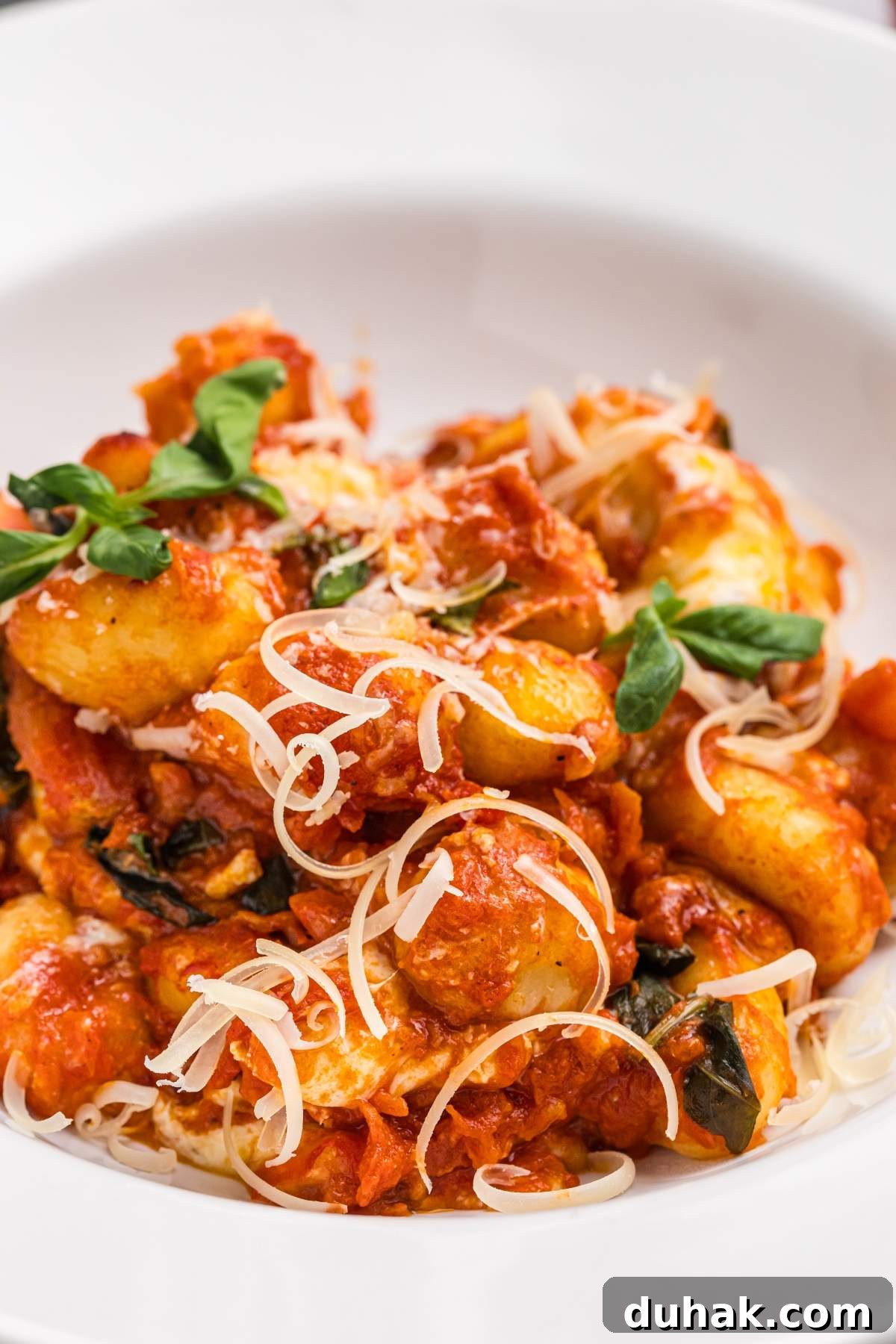 Sorrento-Style Gnocchi with Tomato, Basil & Mozzarella 9 A plate of gnocchi sorrentino in tomato sauce, garnished with grated cheese and fresh basil.