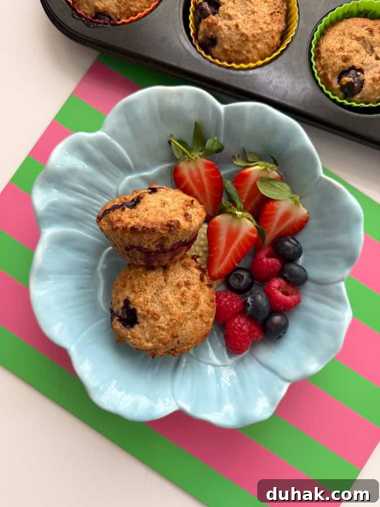 Two muffins in a baby blue,flower shaped bowl, served with fresh berries.