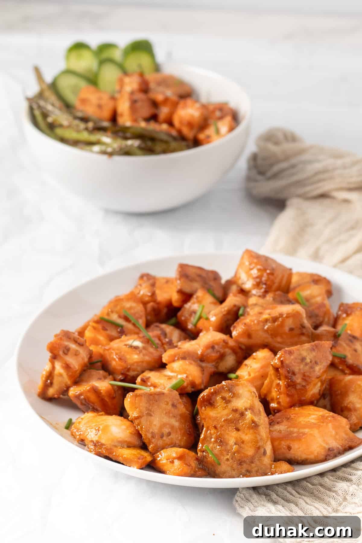 salmon bites on a white plate with a rice bowl in the background.