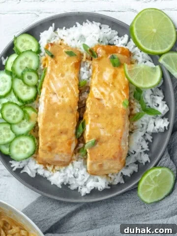 Thai red curry salmon on a bed of rice with limes and cucumbers.