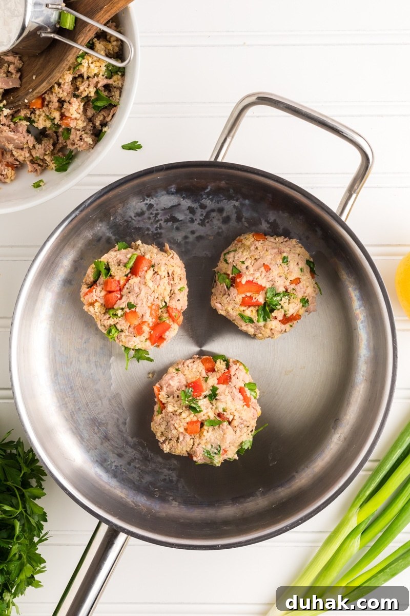 Top down view of three tuna burger patties sitting in a skillet to be cooked - Hostess At Heart