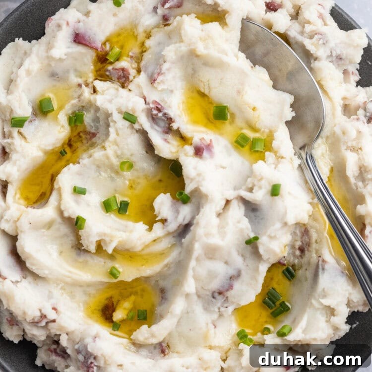 Fluffy, whipped, red skin mashed potatoes in a large blue-grey bowl with a spoon on a holiday table.