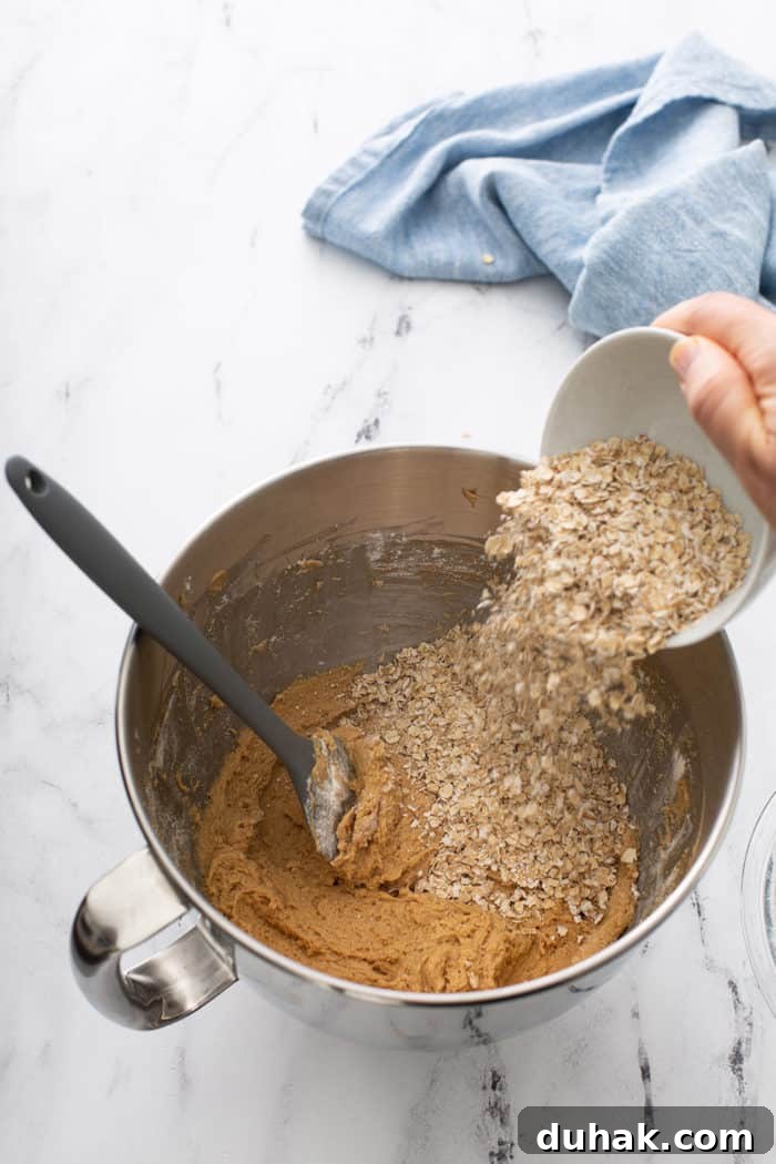 Biscoff Sandwich Cookies Recipe: Crispy Cookies with Lotus Spread Filling 5 Hand pouring quick cooking oats into a mixing bowl of biscoff cookie dough
