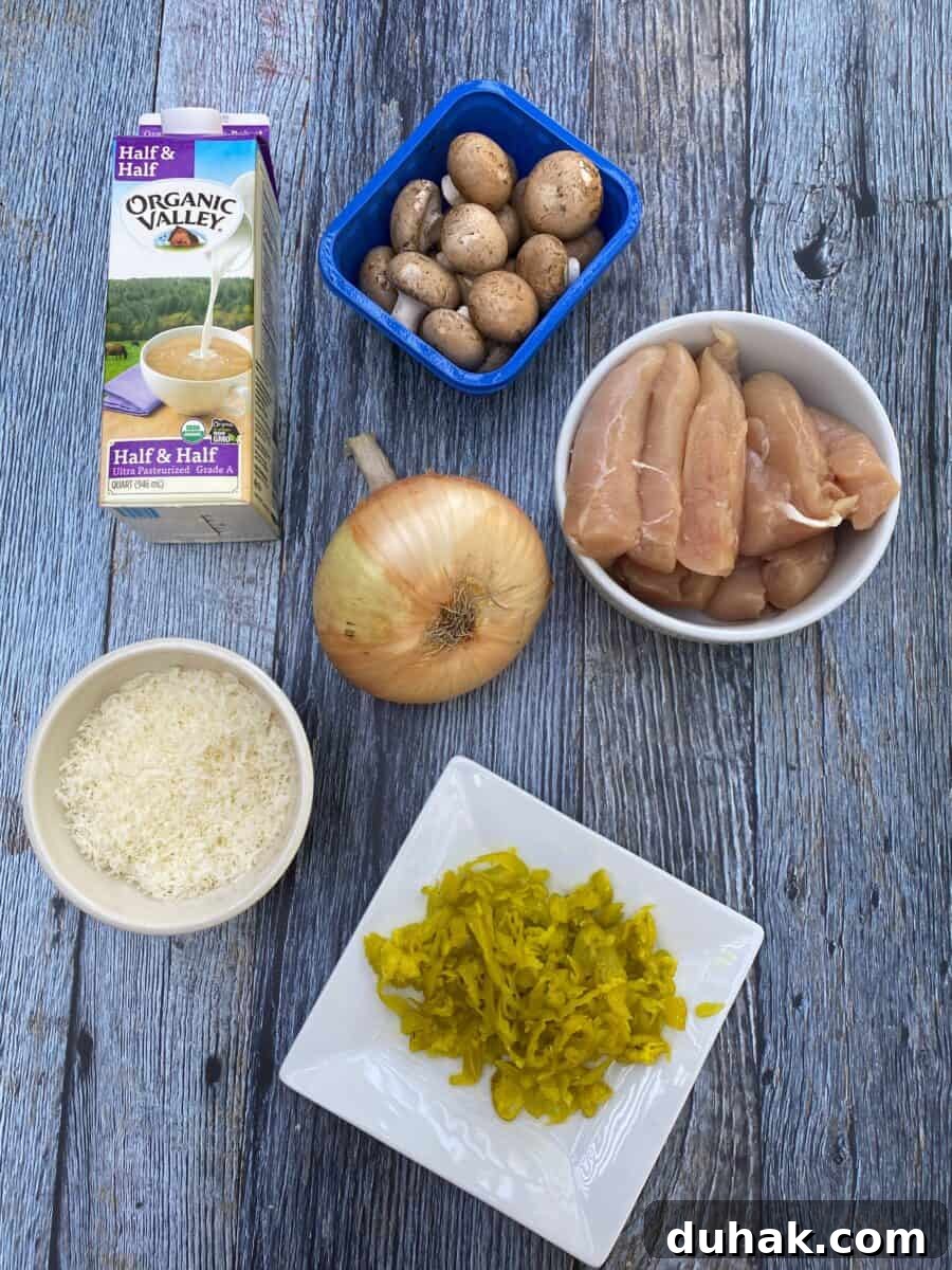 Creamy Spicy Alfredo Sauce Recipe for Pasta and Wings 3 Spicy Chicken Alfredo ingredients on a wooden block, displaying a carton of half and half, mushrooms, uncooked chicken, a sweet onion, grated parmesan cheese and a plate of pepperoncinis.