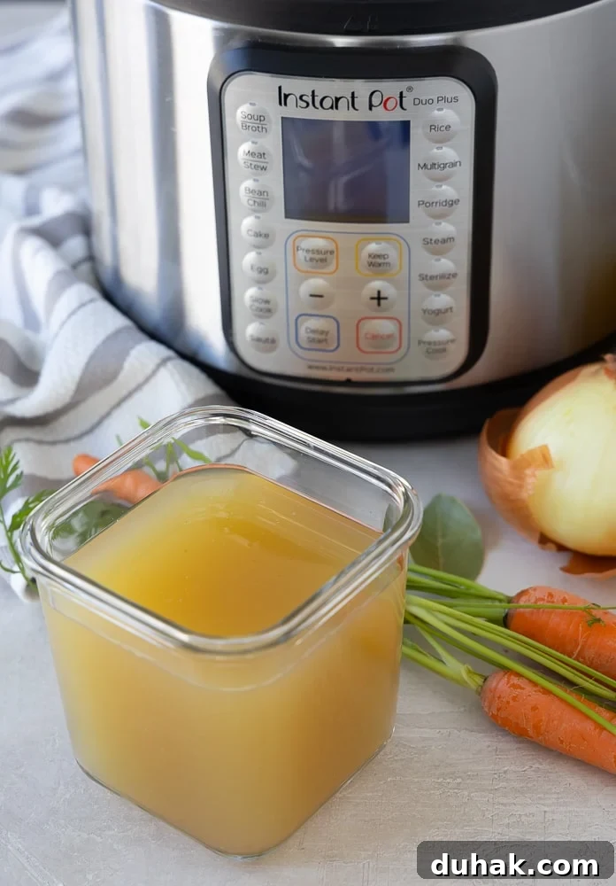 Golden Instant Pot Chicken Broth in a glass container with the pressure cooker behind it. 