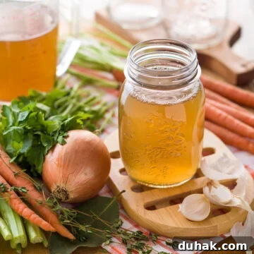 Golden homemade broth on a counter with onions, carrots, celery, and parsley.