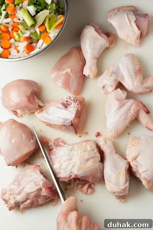 Pieces of a whole cut up chicken ready to use to make broth, with celery, carrots, onion, and herbs.