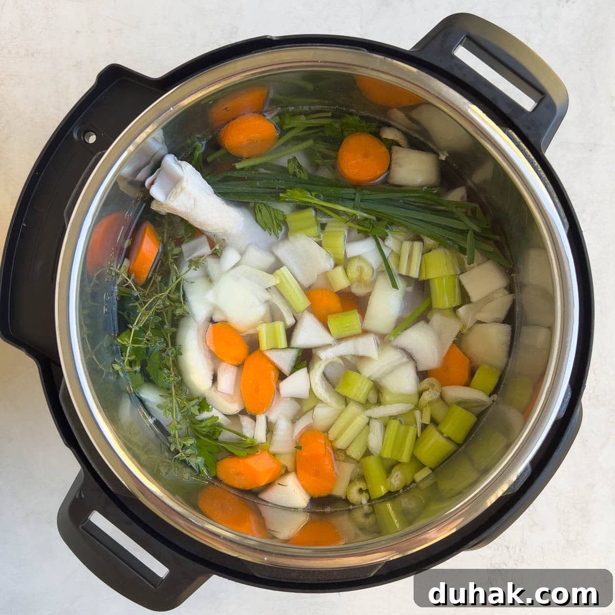 View into an Instant Pot for making chicken broth with chicken, vegetables, and herbs. 