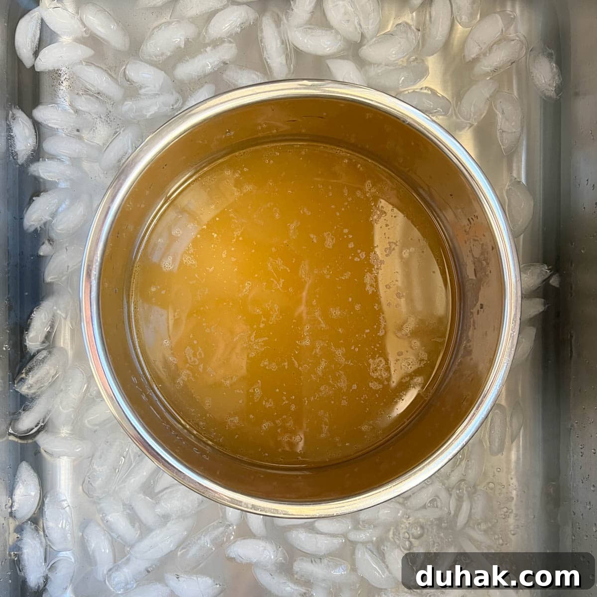 A pot of golden finished chicken broth cooling in a sink full of ice and water. 