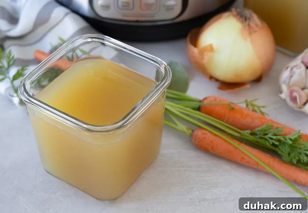 Finished broth in a glass container for freezing, with fresh vegetables alongside.