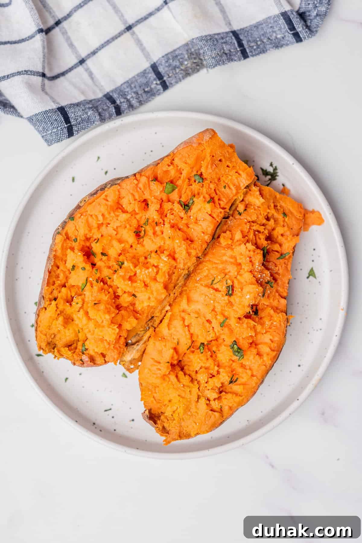 How to Cook a Sweet Potato in the Microwave Fast 2 An overhead image of a microwaved sweet potato open in half sprinkled with fresh herbs.