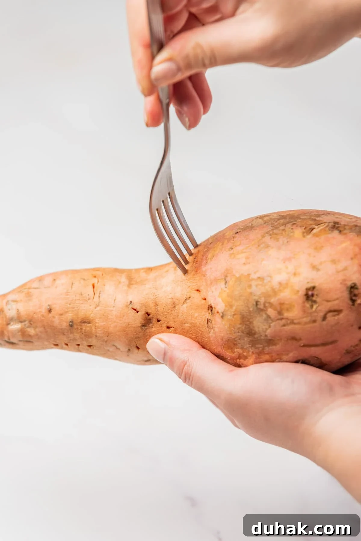 How to Cook a Sweet Potato in the Microwave Fast 4 An image of a hand holding a sweet potato while being pierced by a fork.