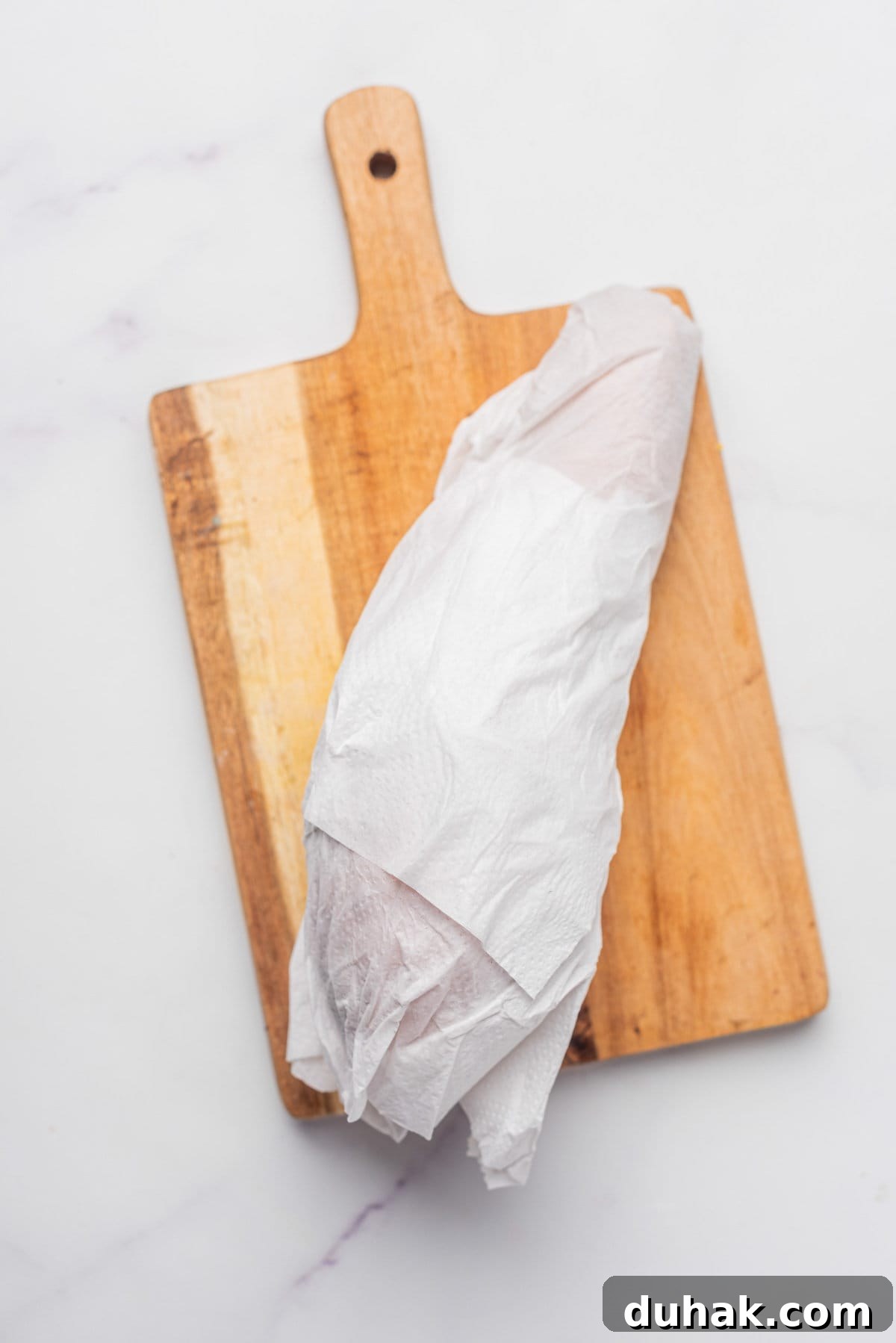 How to Cook a Sweet Potato in the Microwave Fast 5 An image of sweet potato wrapped in a paper towel while resting on a chopping board.