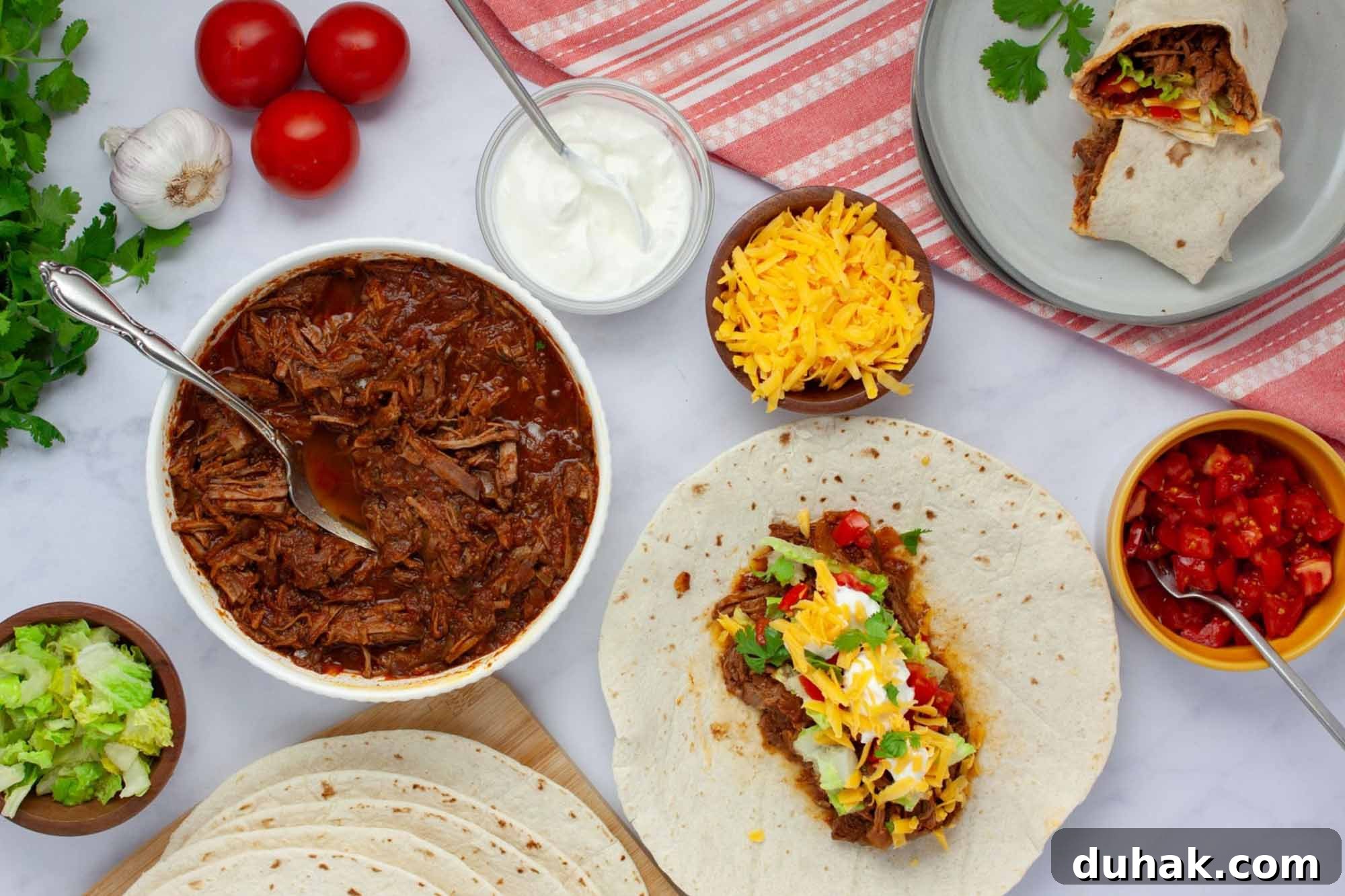 Slow-Cooked Seasoned Beef Burritos for the Crockpot 2 Overhead view of slow cooker beef burrito meat in a bowl surrounded by garnishes, tortillas, and a plate with a half-assembled burrito.