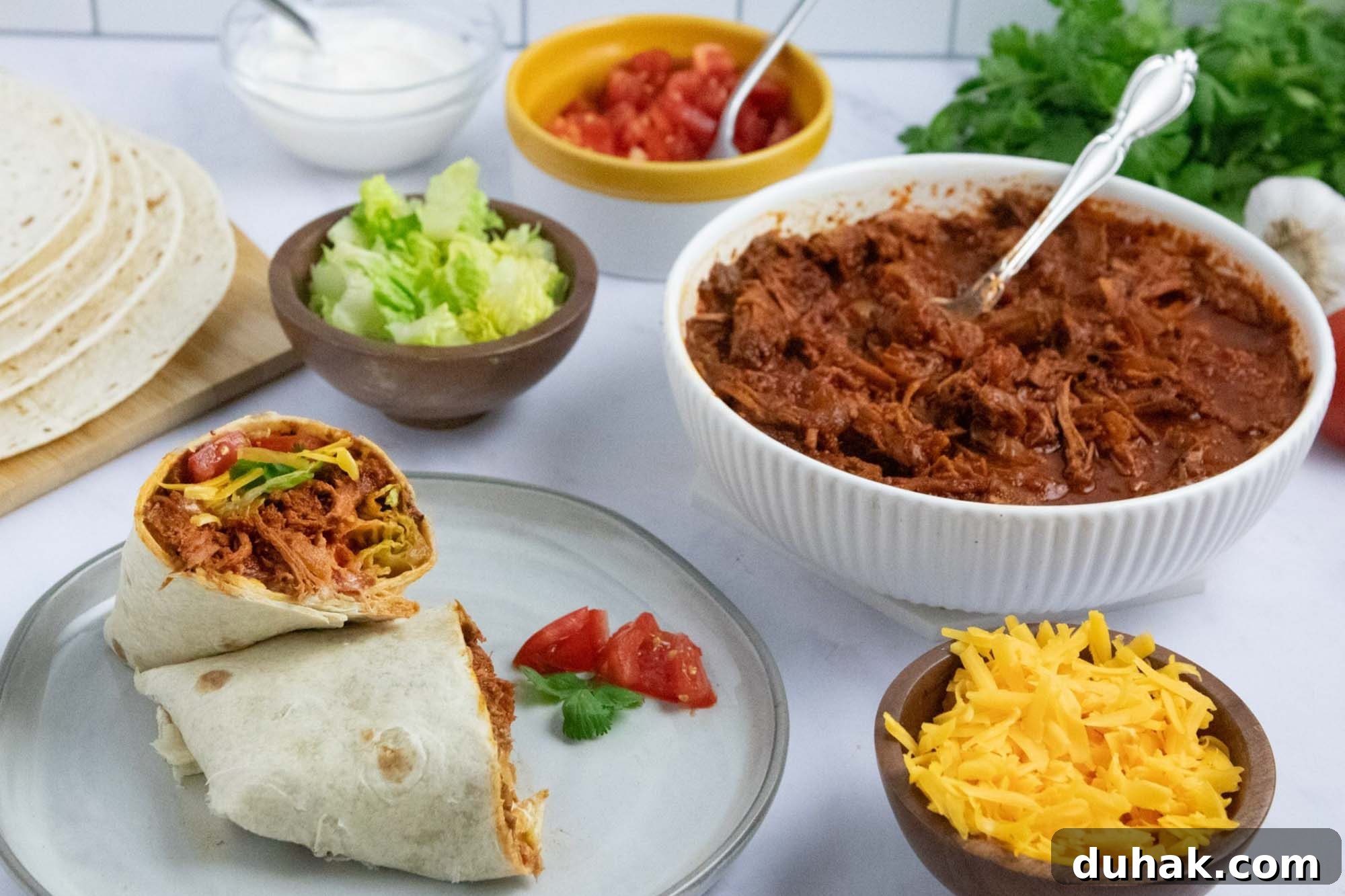 Slow-Cooked Seasoned Beef Burritos for the Crockpot 7 Overhead view of slow cooker beef burrito meat in a bowl surrounded by garnishes, tortillas, and a plate with an assembled burrito.
