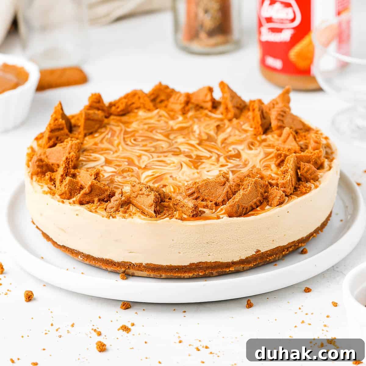 Biscoff Cheeecake topped with chunks of biscoff cookies on a white plate over a white surface,