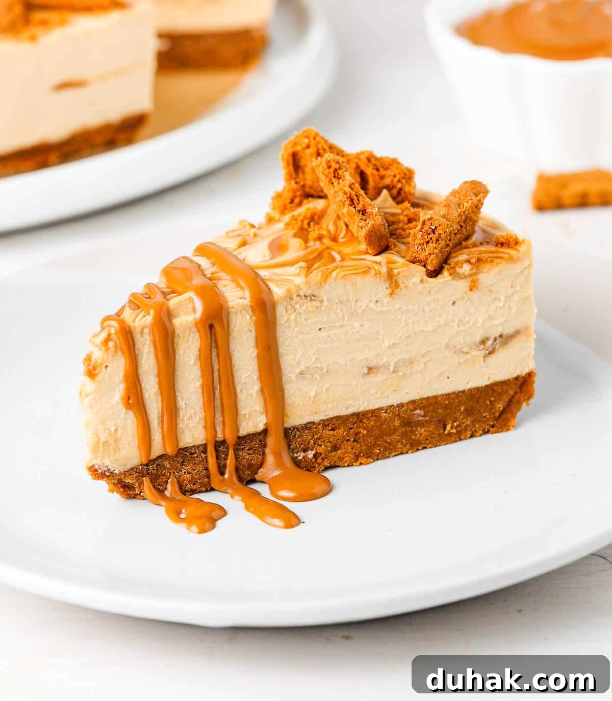 One slice of cake drizzled with biscoff on a small white plate.