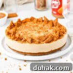 Biscoff Cheeecake topped with chunks of biscoff cookies on a white plate over a white surface,
