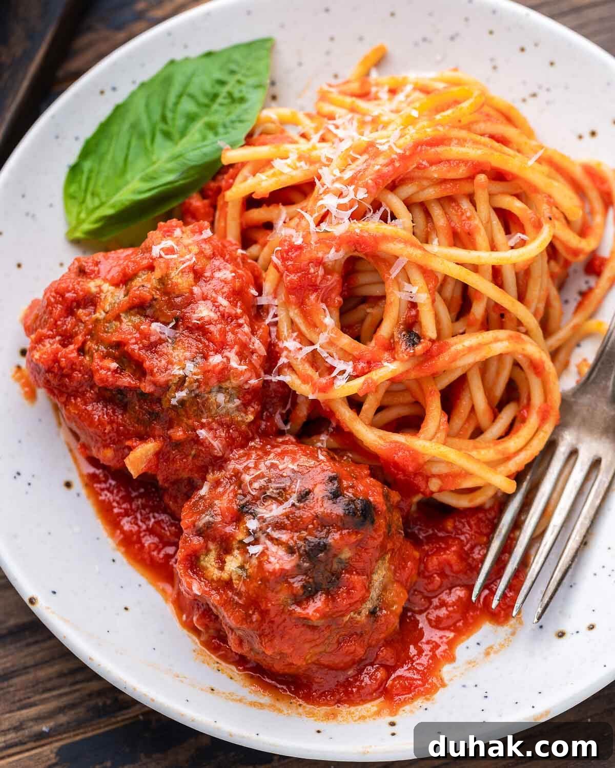 Spaghetti and meatballs on white plate with basil garnish.