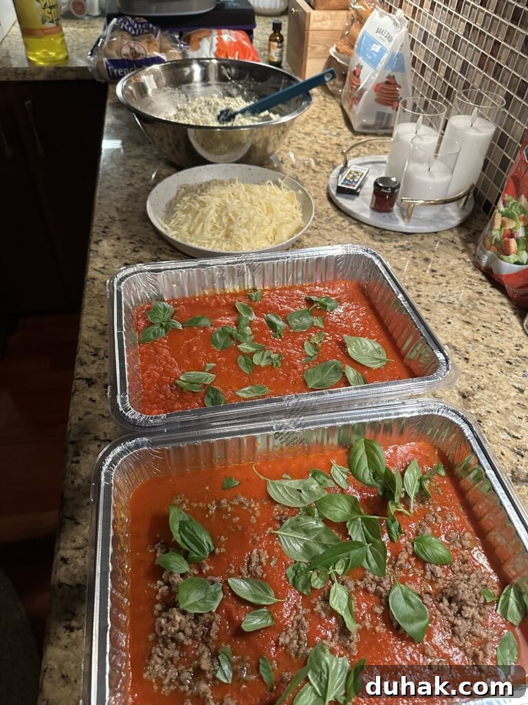 Authentic Italian Lasagna Recipe for Rich, Homemade Flavor 7 A station set up on the kitchen counter with everything needed to prepare the lasagna, including a bowl of cheese mixture, a bowl of shredded cheese, and aluminum tins with tomato sauce and basil, one with sausage and one without