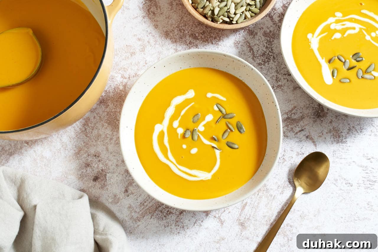 Gochujang Kabocha Squash Soup with Coconut Cream 2 Two bowls of kabocha squash soup topped with a drizzle of heavy cream and pumpkin seeds, a large pot of soup is in the upper left, a bowl of pumpkin seeds is at the top.