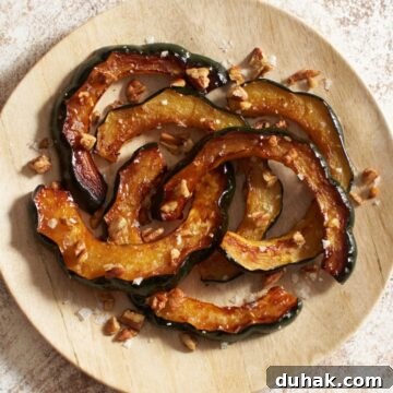 An oval plate of maple roasted acorn squash topped with pecans and flaky sea salt.