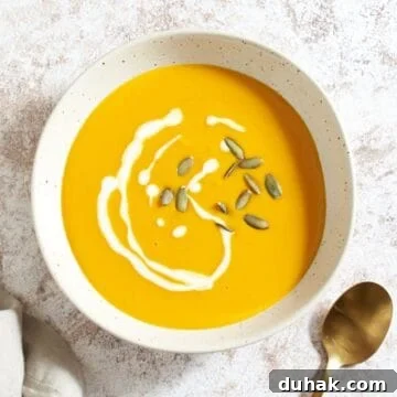 Gochujang Kabocha Squash Soup with Coconut Cream 12 A bowl of kabocha squash soup topped with a drizzle of heavy cream and pumpkin seeds, a gold spoon is on the right.