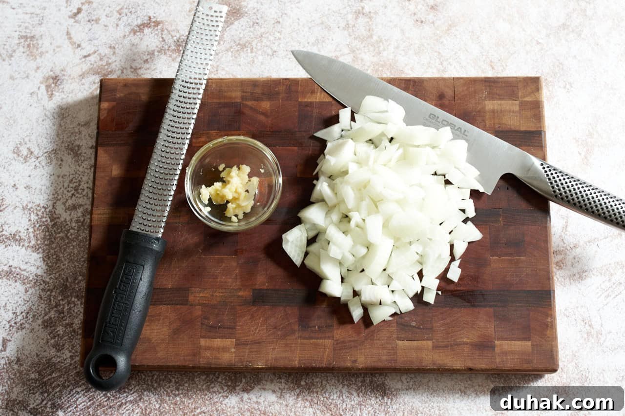 Gochujang Kabocha Squash Soup with Coconut Cream 5 Diced onion and a small bowl of grated garlic on a cutting board with a knife and a microplane grater.
