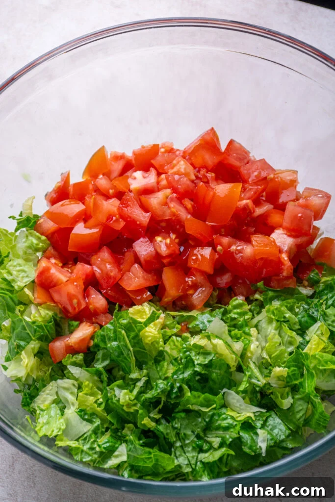 Adding diced tomatoes to the bowl with lettuce.