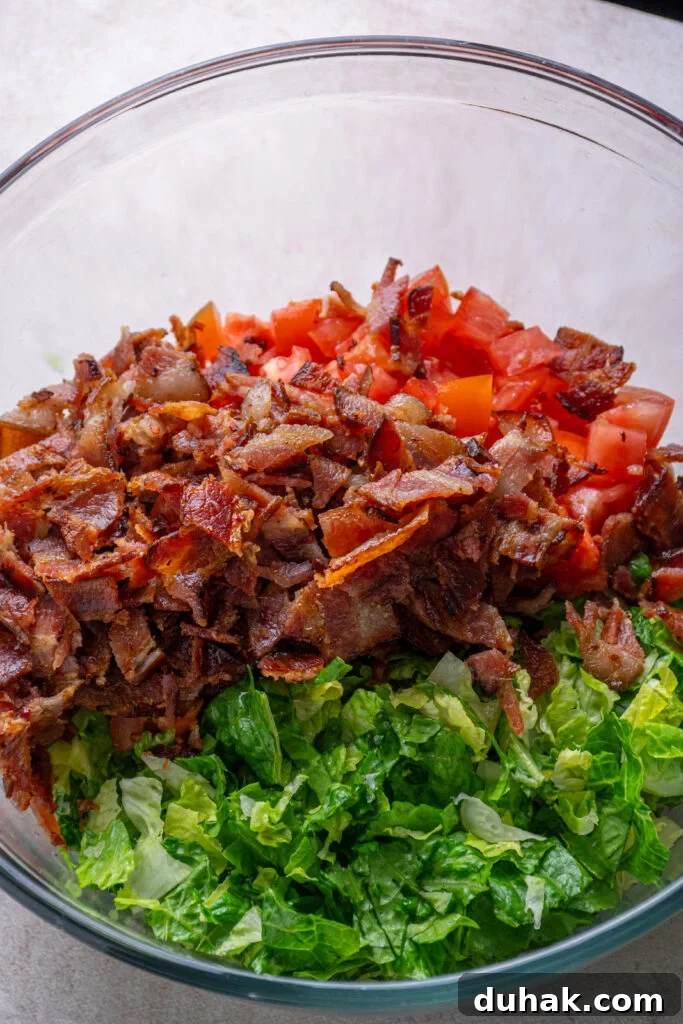 Adding bacon to the bowl with the lettuce and tomatoes.