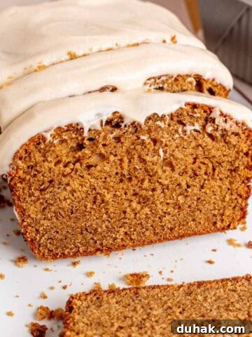 A loaf of spice cake with brown butter cream cheese frosting cut into slices.
