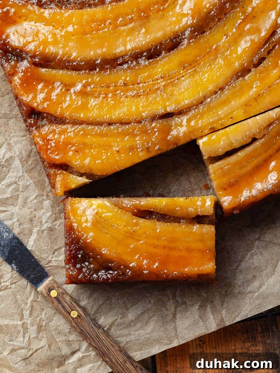 gluten free banana upside down cake. a moist banana cake topped with brown sugar caramelized bananas, on parchment paper with a small knife next to it