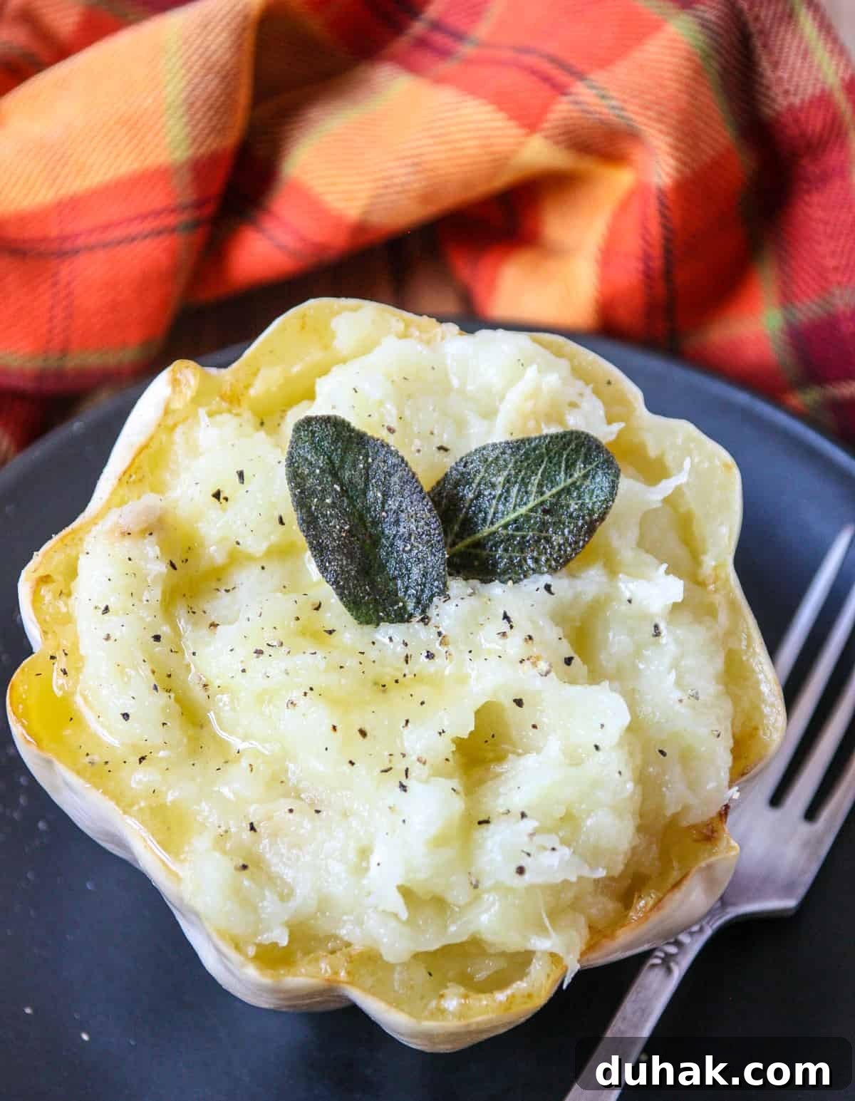 Mashed squash in its shell on a black plate, garnished with fried sage leaves.