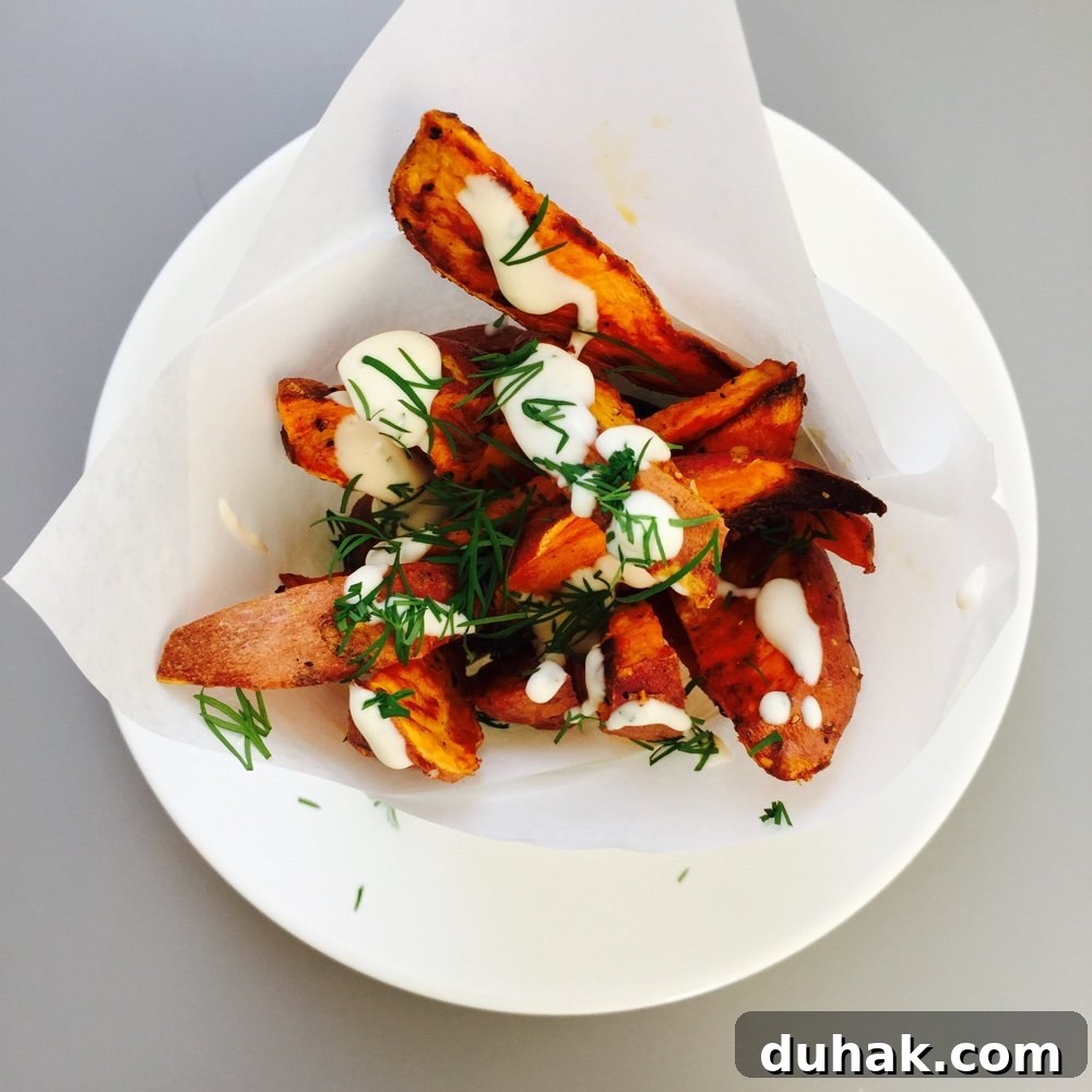 a paper cone of sweet potato wedges with lemon-y mayonnaise drizzled over them and chopped dill scattered over.