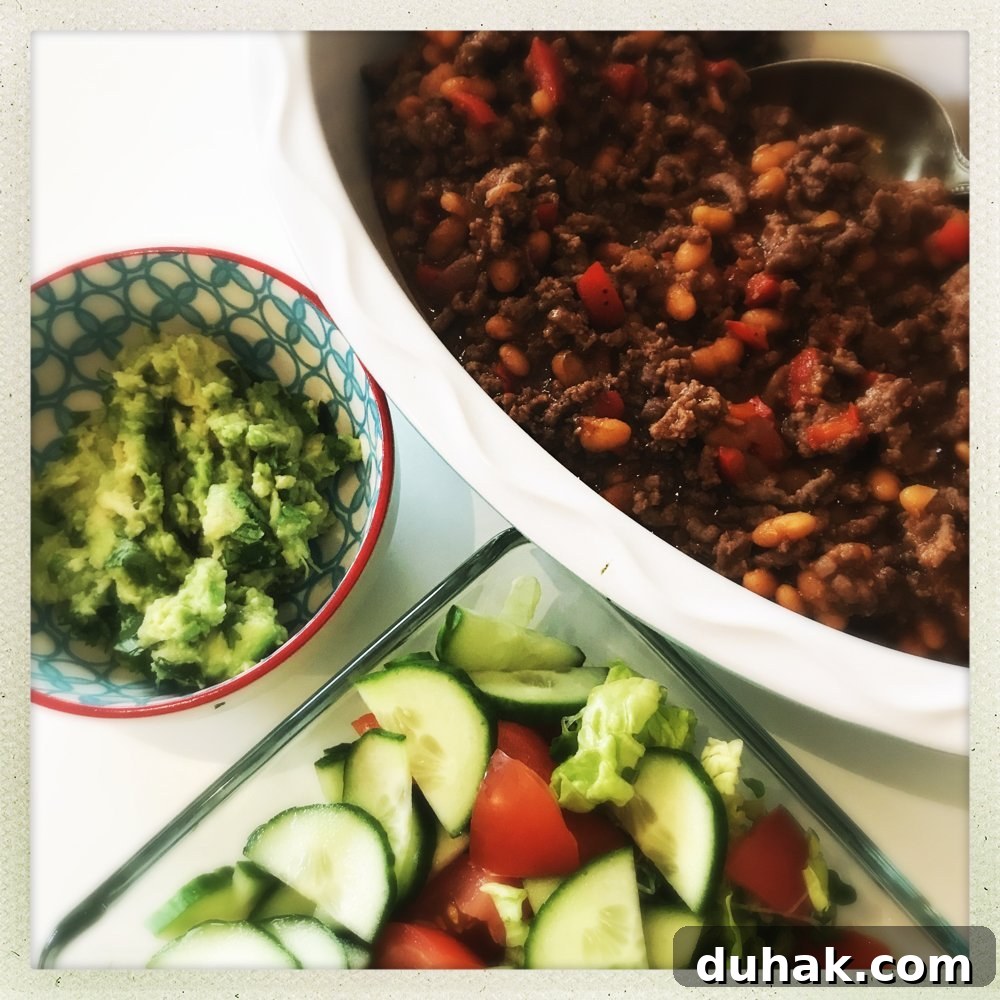 bowl of 20 minute beef and baked bean chilli alongside homemade guacamole and green salad